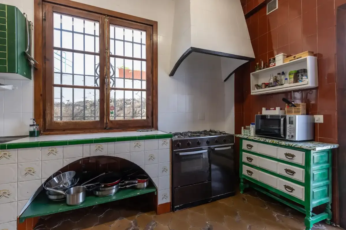 A kitchen with a stove beneath a large range hood and a window.