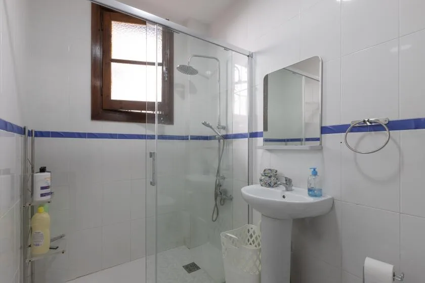 A tiled bathroom with a glass shower, a sink, and a window.