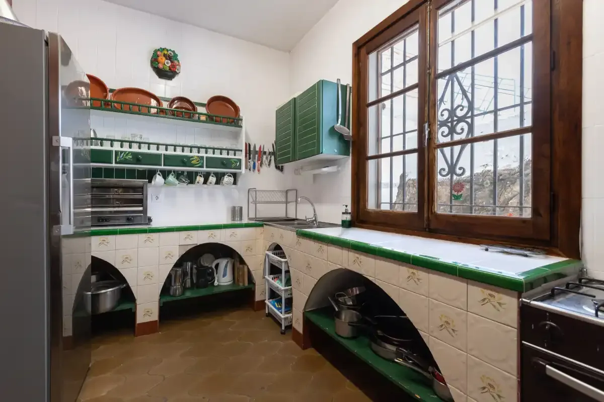 A kitchen with green countertops, tiled surfaces, and a large wood-framed window.