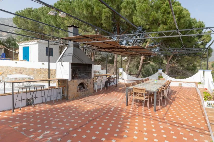 An outdoor terrace with dining tables and a built-in barbecue beneath a canopy.