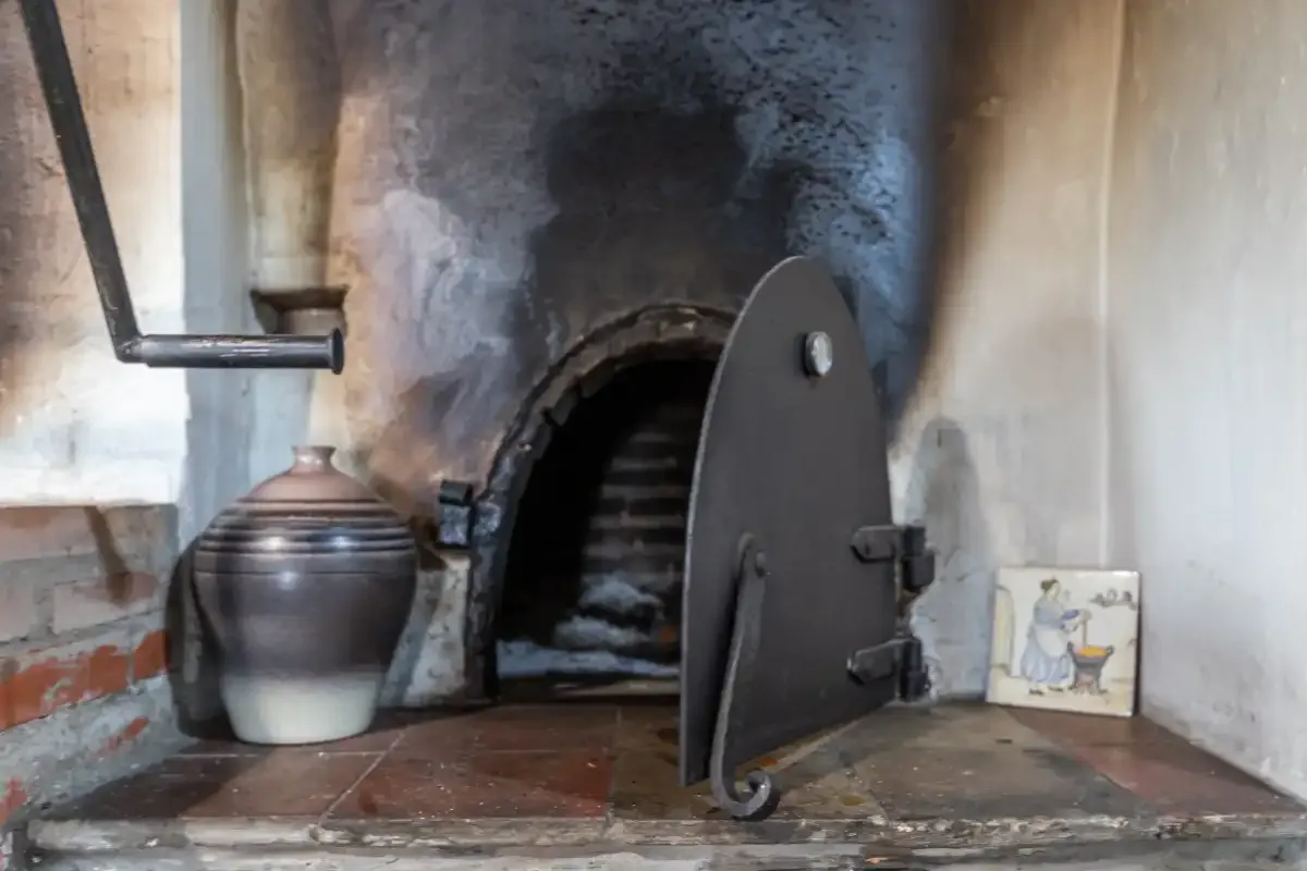 A rustic brick oven with its metal door open in a stone wall.