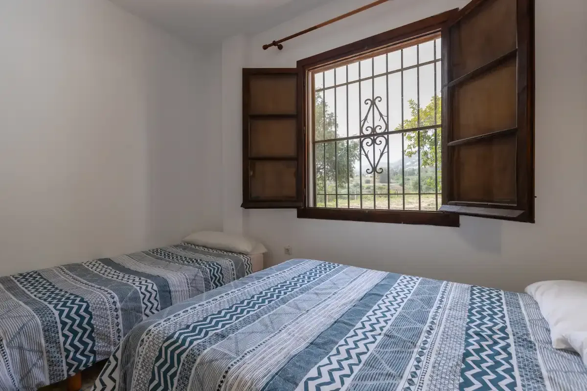 A bedroom with two beds beneath an open window with decorative bars.