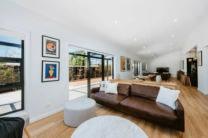 A bright open-plan living room with brown seating and large glass doors.