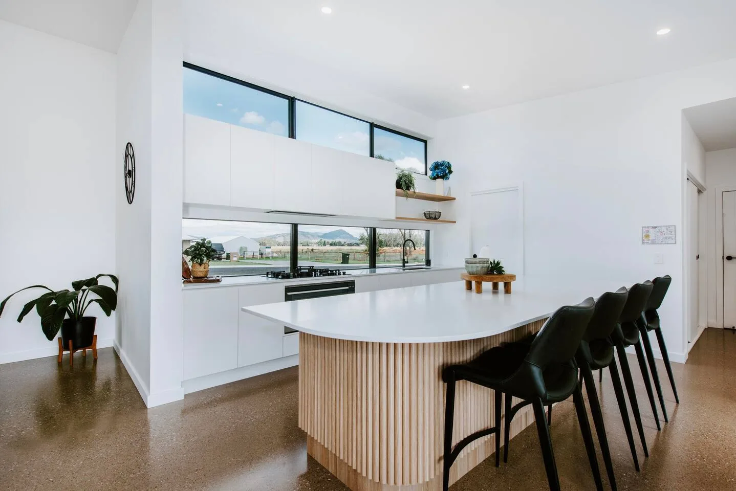 A bright modern kitchen has a long island with bar seating and large windows.