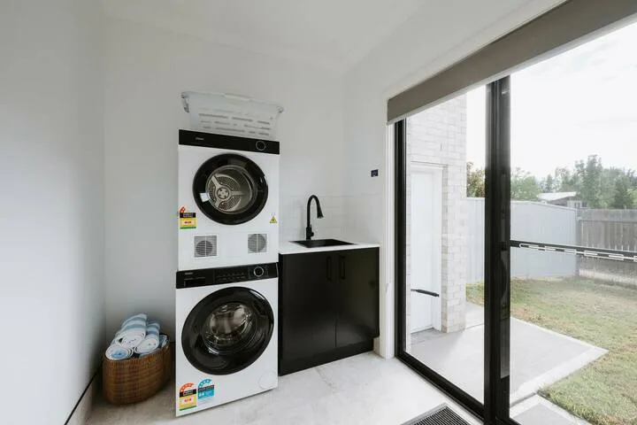 A laundry area with a stacked washer and dryer beside a dark counter and sink.