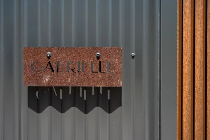 A metal sign reading “Capriille” is mounted on a corrugated wall beside a wooden frame.