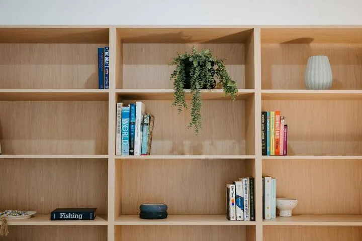 A wooden bookshelf displays books, a potted plant, and decorative objects.