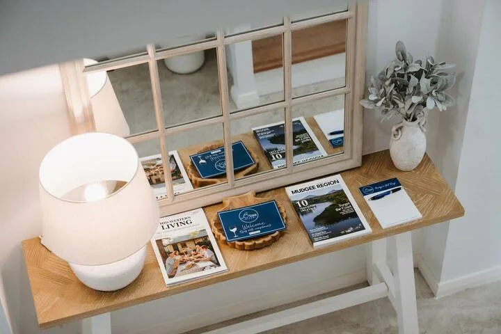 A wooden console table displays brochures beside a lamp and a vase of dried flowers.