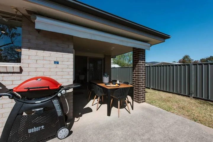 A covered patio with outdoor seating and a barbecue beside a fenced yard.