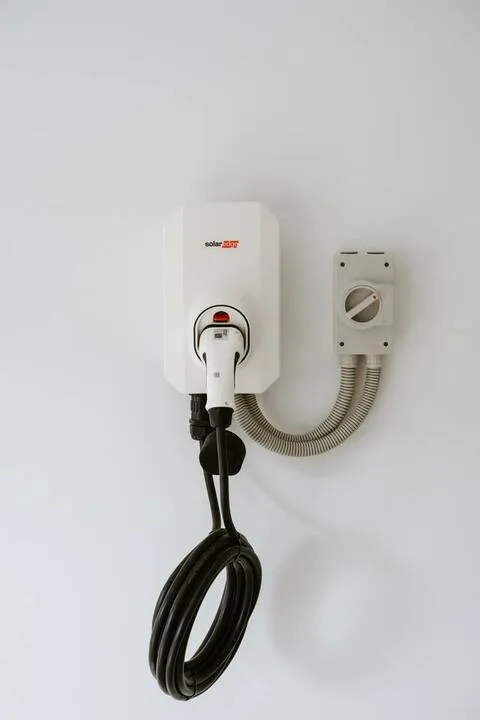 A wall-mounted device with a coiled black cable is shown against a white wall.