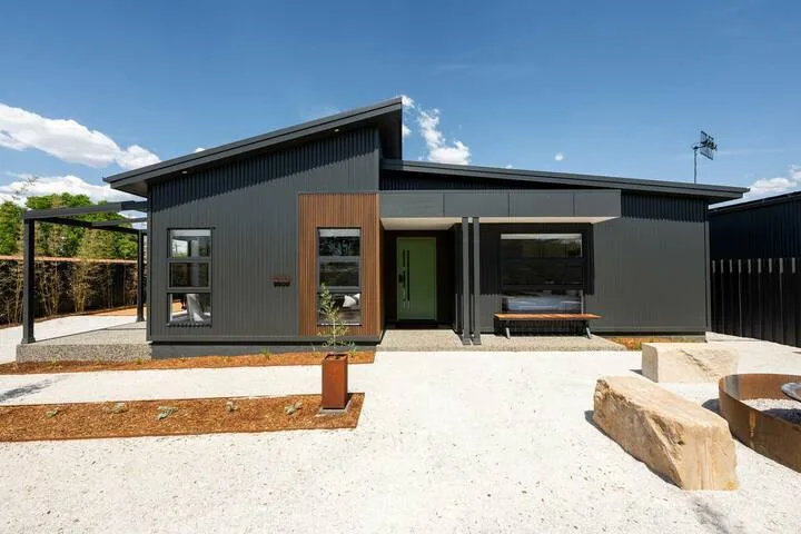 A modern dark-clad house faces a pale gravel courtyard with a built-in bench.