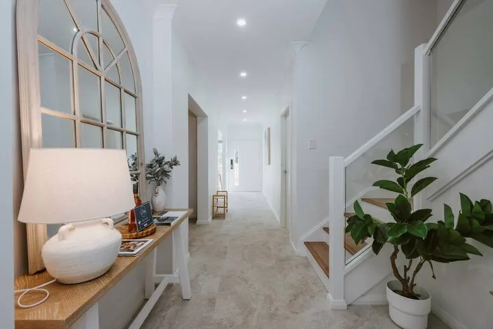 A bright hallway with a staircase and a console table beside an arched window.