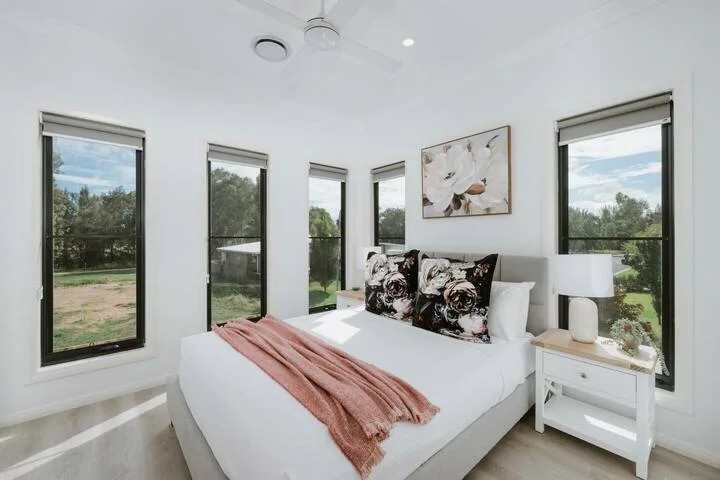 A bright bedroom with a bed dressed in white linens and a pink throw.