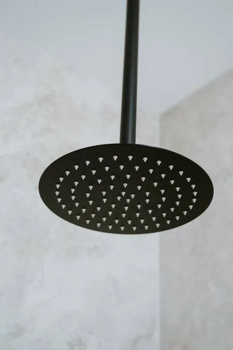 A bathroom shower head is mounted against a light-colored tiled wall.