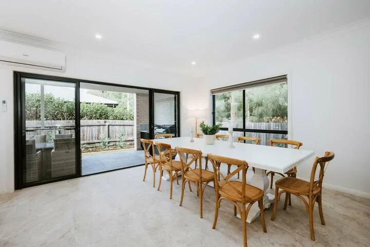 A bright dining area with a long table and wooden seating beside large windows.