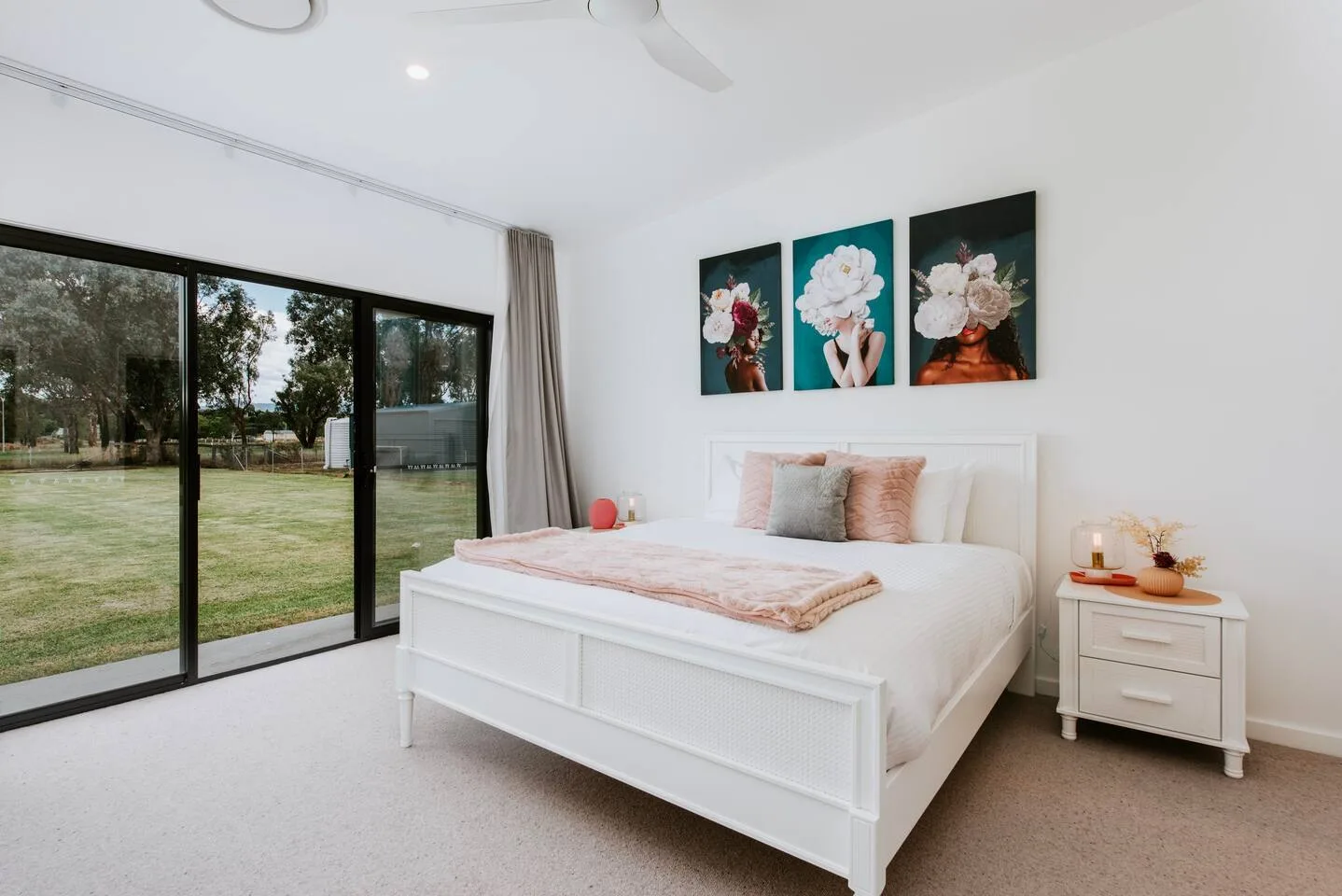 Un dormitorio luminoso con una cama blanca junto a grandes puertas de vidrio que dan al césped.