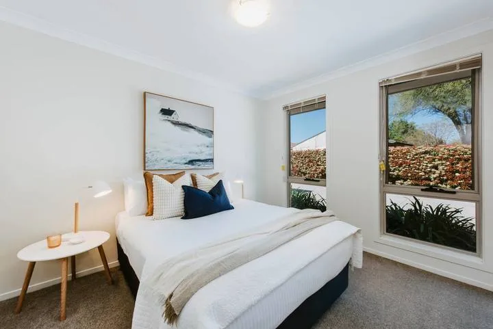 A bright bedroom with a neatly made bed and large windows overlooking greenery.