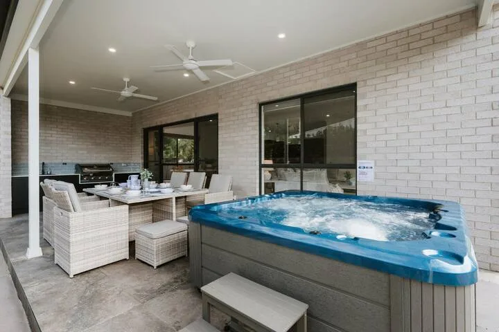 A covered patio has outdoor dining seating beside a bubbling hot tub.