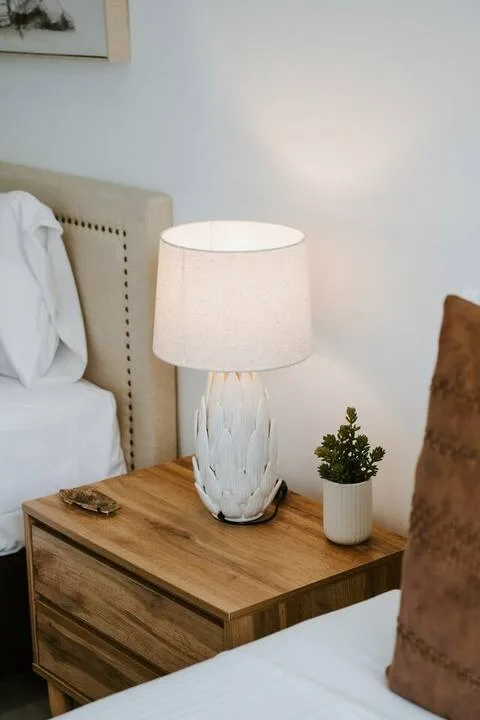 A bedroom with a wooden bedside table, lamp, and small potted plant.