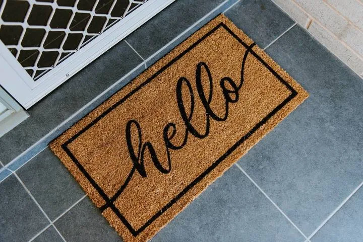 A welcome mat lies on a tiled entryway floor beside a patterned door.