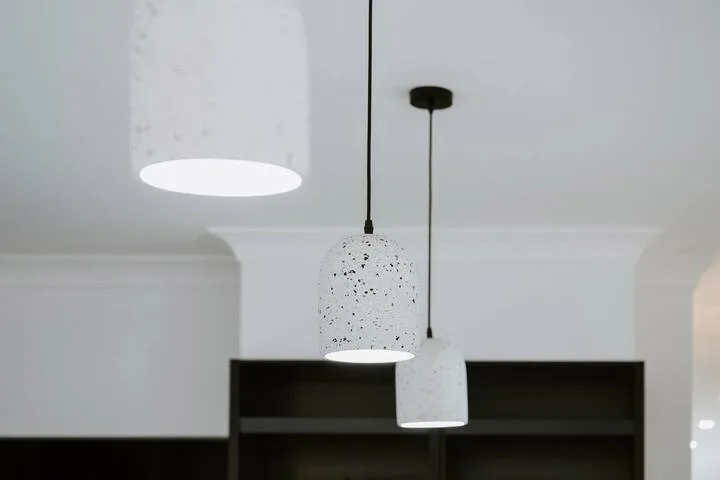 A bright interior ceiling with three pendant lights above dark shelving.