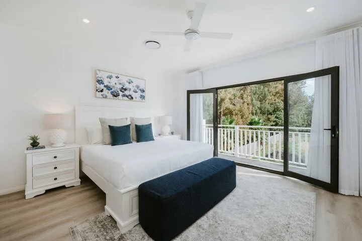 A bright bedroom with a white bed and glass doors opening onto a balcony.