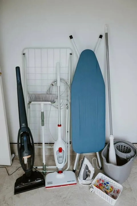 Cleaning supplies and an ironing board are arranged against a wall.
