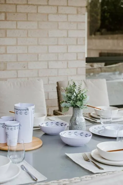 A dining table is set with white dishes and a small floral arrangement.