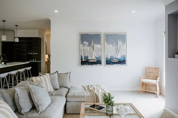 A bright living room with a gray sectional, glass coffee table, and sailboat artwork.