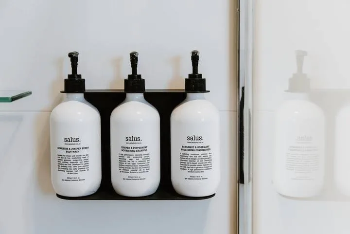 Bathroom wall with three mounted pump bottles beside a mirror.