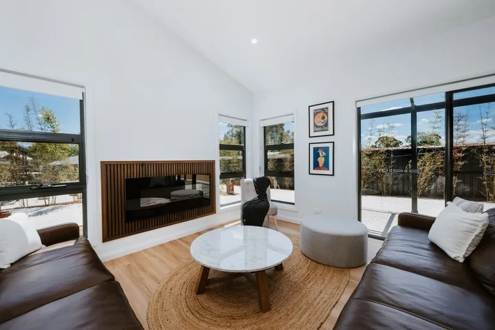 A bright living room has dark seating, a round coffee table, and large windows.