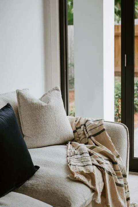 A seating area by tall windows has light cushions and a draped blanket.
