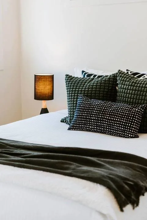 A neatly made bed has dark textured pillows and a folded blanket.