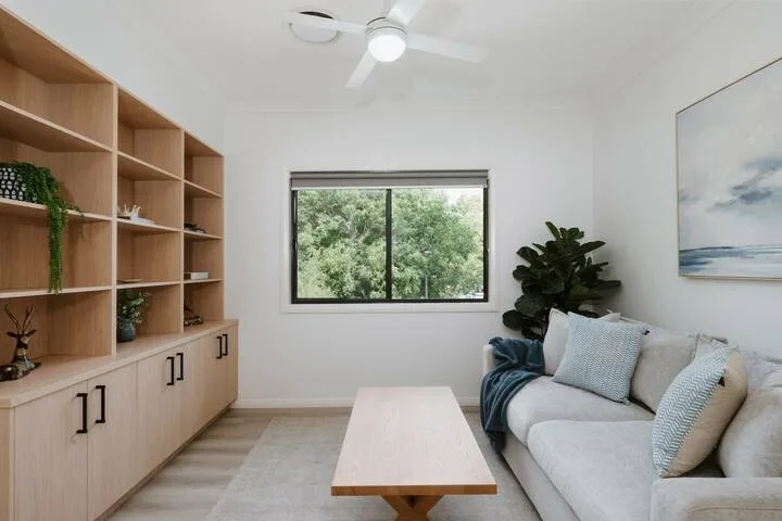 A bright living room with a sofa, wooden shelving, and a large window.