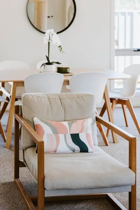 A bright dining area with a cushioned armchair in the foreground and a table behind it.