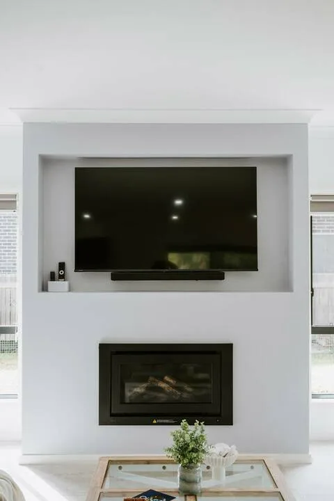 A bright living room features a television above a fireplace and a glass coffee table.