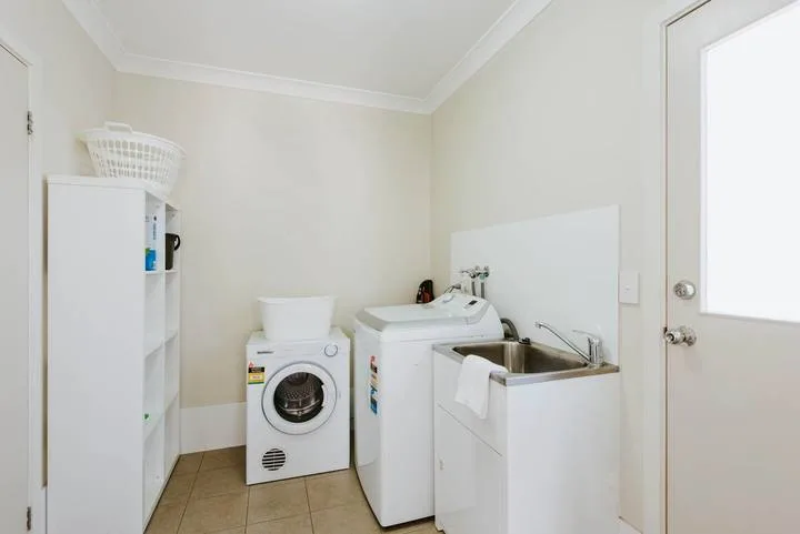 A laundry room with washing machines, a sink, and storage shelves.