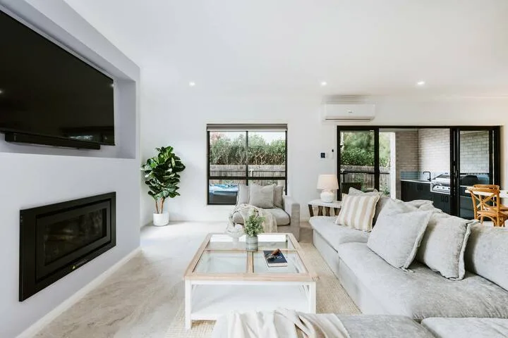 A bright living room with a fireplace, seating, and windows overlooking greenery.