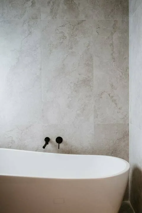 A freestanding bathtub sits against a tiled bathroom wall.