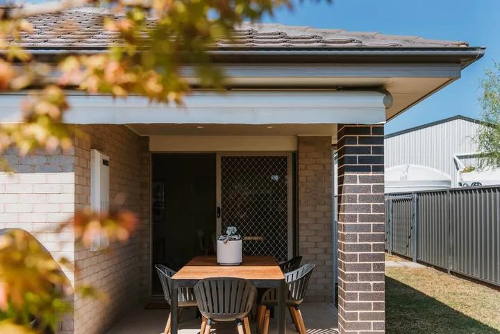 A brick patio with an outdoor dining table sits beside a house.