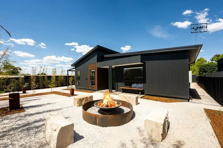 A modern dark-sided building opens onto a paved patio with a fire pit.