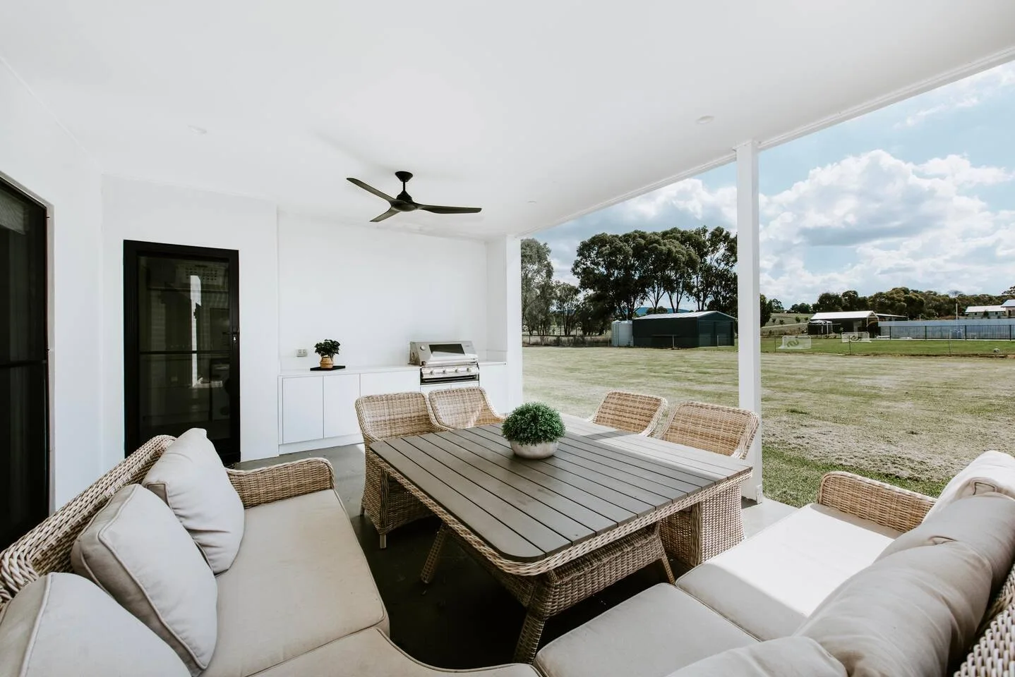 Un patio cubierto con asientos acolchados y una mesa de comedor da a una zona verde abierta.