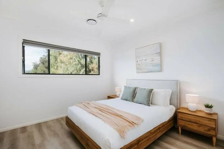A bright bedroom with a wooden bed beneath a window.
