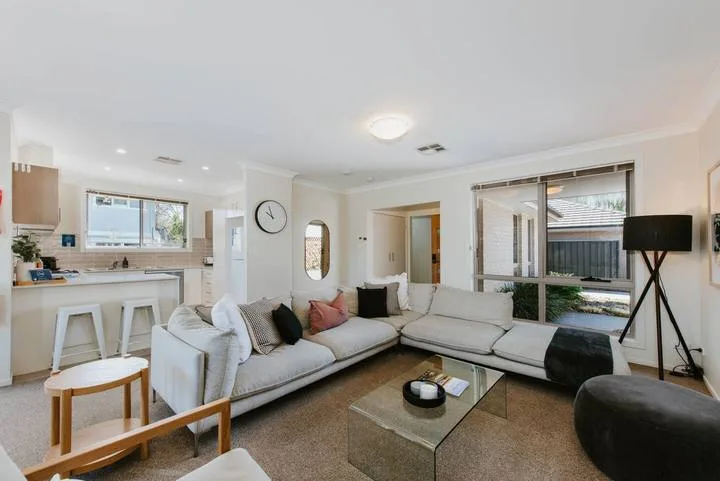 A bright living room with sectional seating and a kitchen counter in the background.