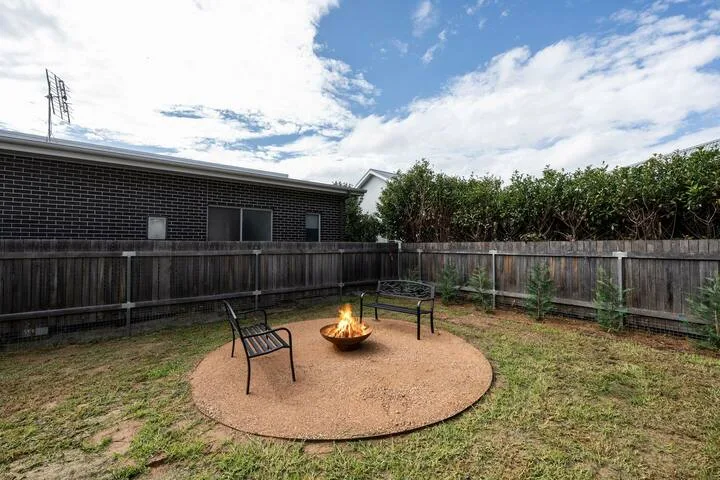 A fenced backyard with a circular patio, outdoor seating, and a fire pit.
