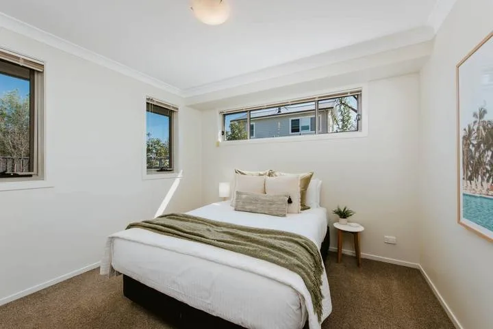 A bright bedroom with a bed, narrow windows, and framed wall art.