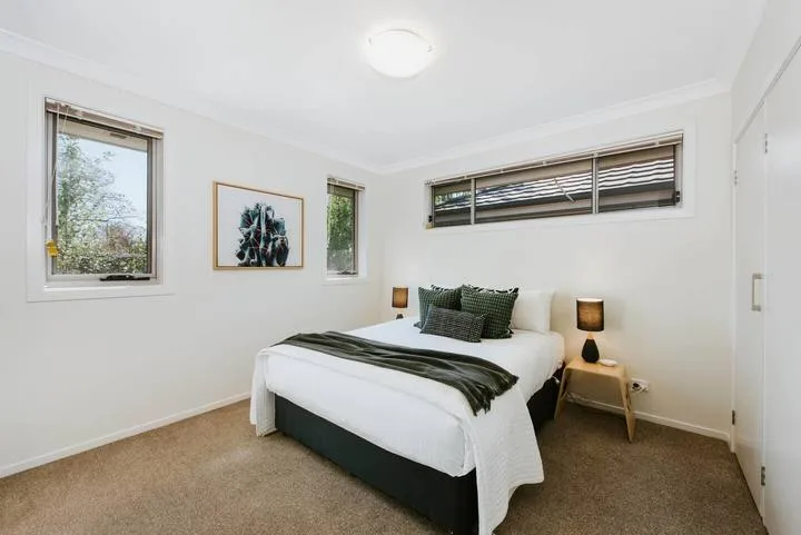 A bedroom with a bed, bedside tables, and windows.