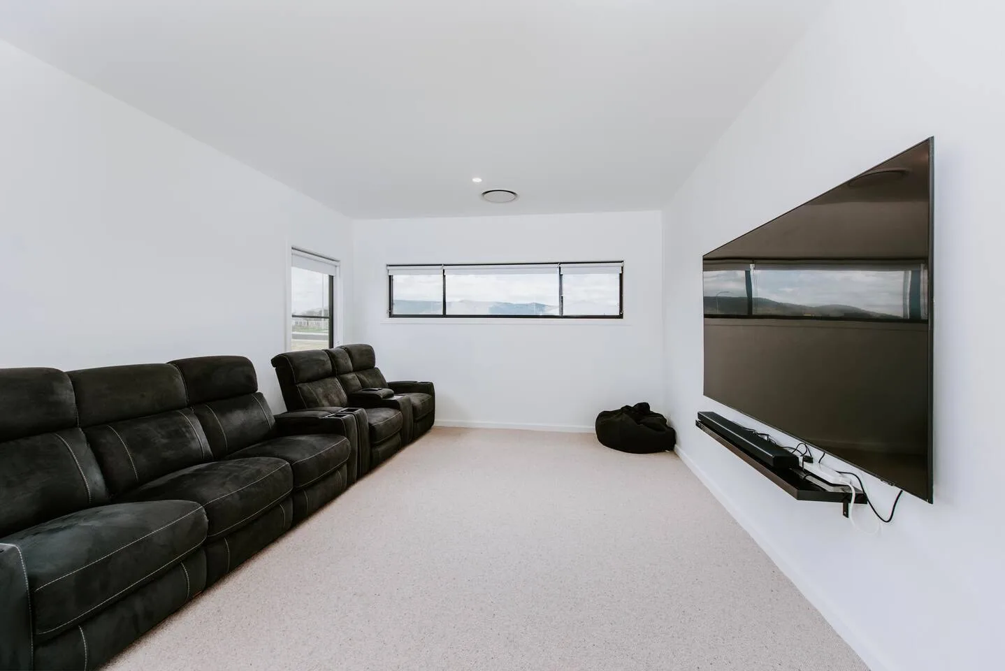 A media room has dark seating and a large television mounted on the wall.