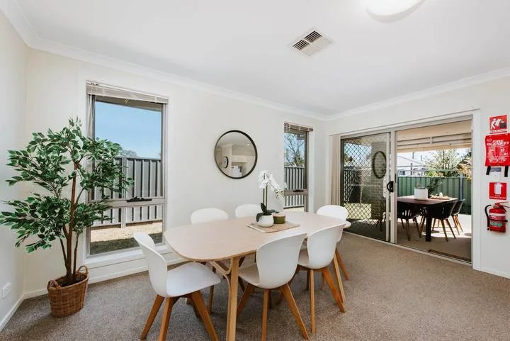 A bright dining area with a table and white seating beside windows and a patio.
