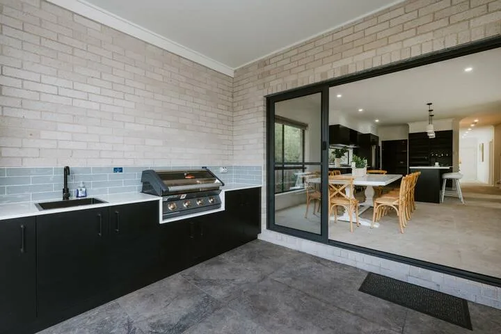 A covered outdoor kitchen opens onto a dining area through large sliding glass doors.